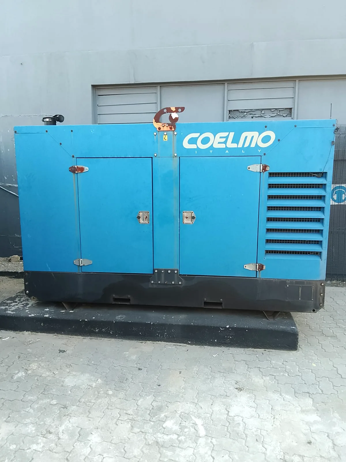 Blue Coelmo diesel generator set on a concrete plinth outside an industrial building
