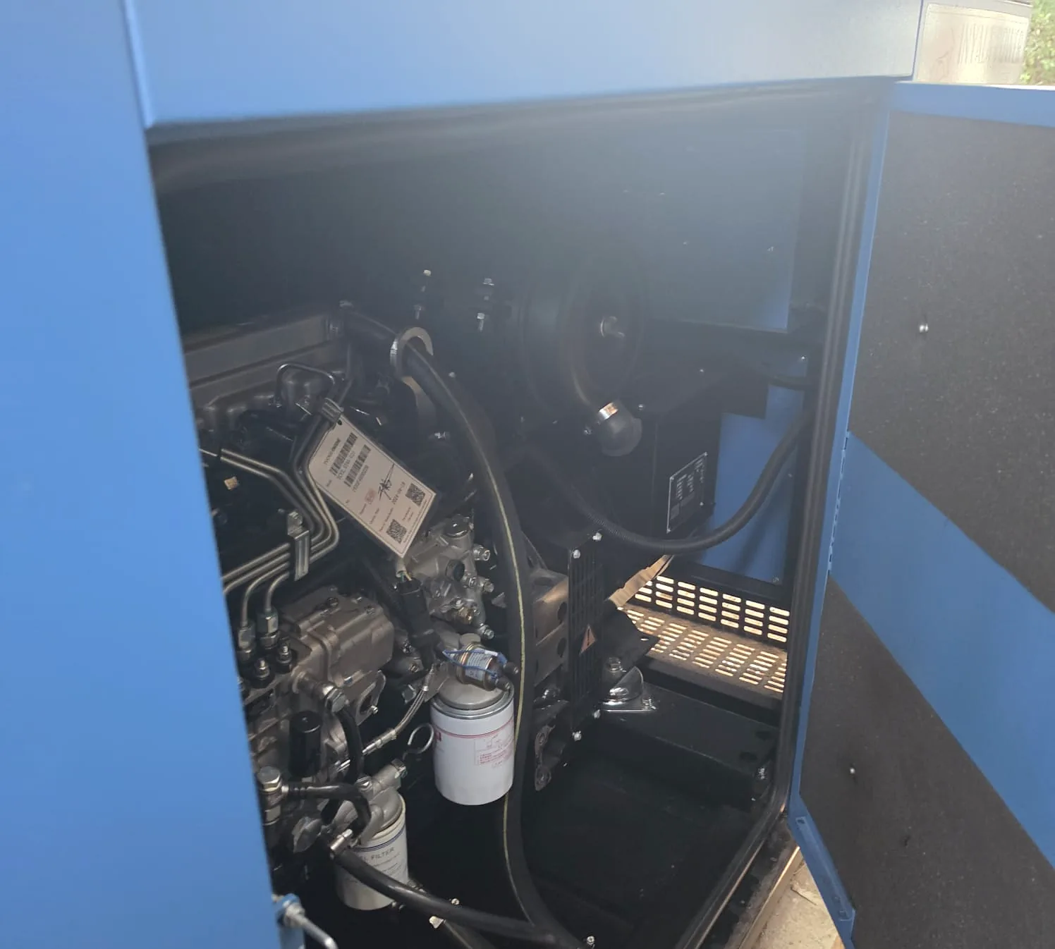 Diesel engine inside a blue generator canopy with the door open, showing injection lines and filters