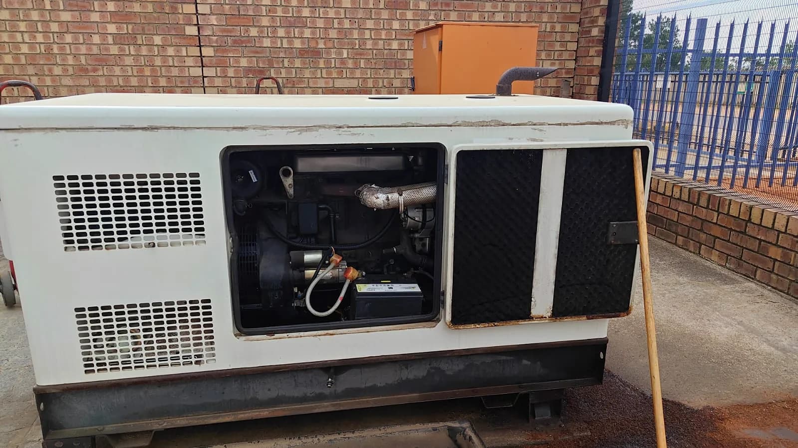 Open service door of a diesel generator showing the engine, starter motor and cables, and the starting battery