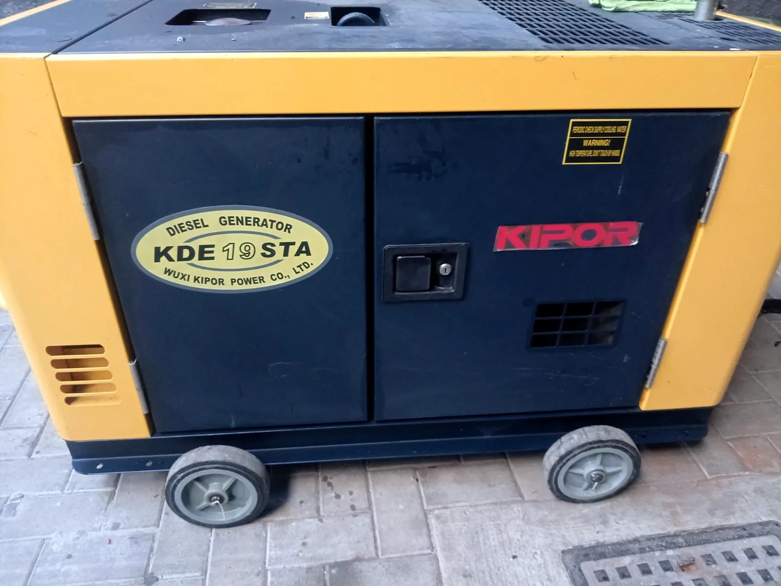Kipor KDE19STA silent diesel generator with a yellow and black canopy, on wheels on paving