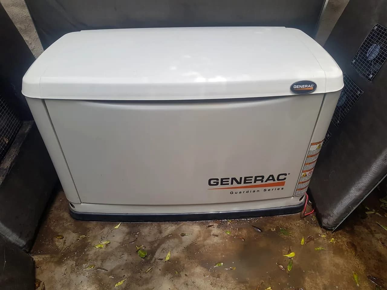 Generac Guardian Series home standby generator in an enclosed corner, on a concrete floor with fallen leaves