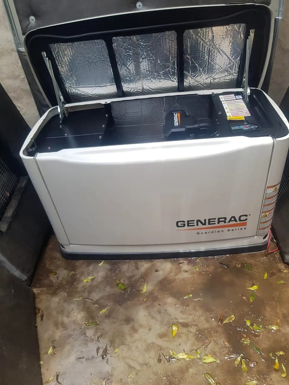 Generac Guardian standby generator with its lid raised, on a damp concrete floor