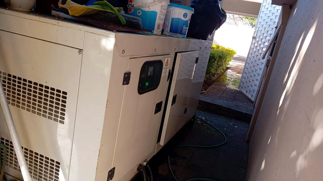 Silent diesel generator squeezed into a narrow passage, with household items stacked on its canopy