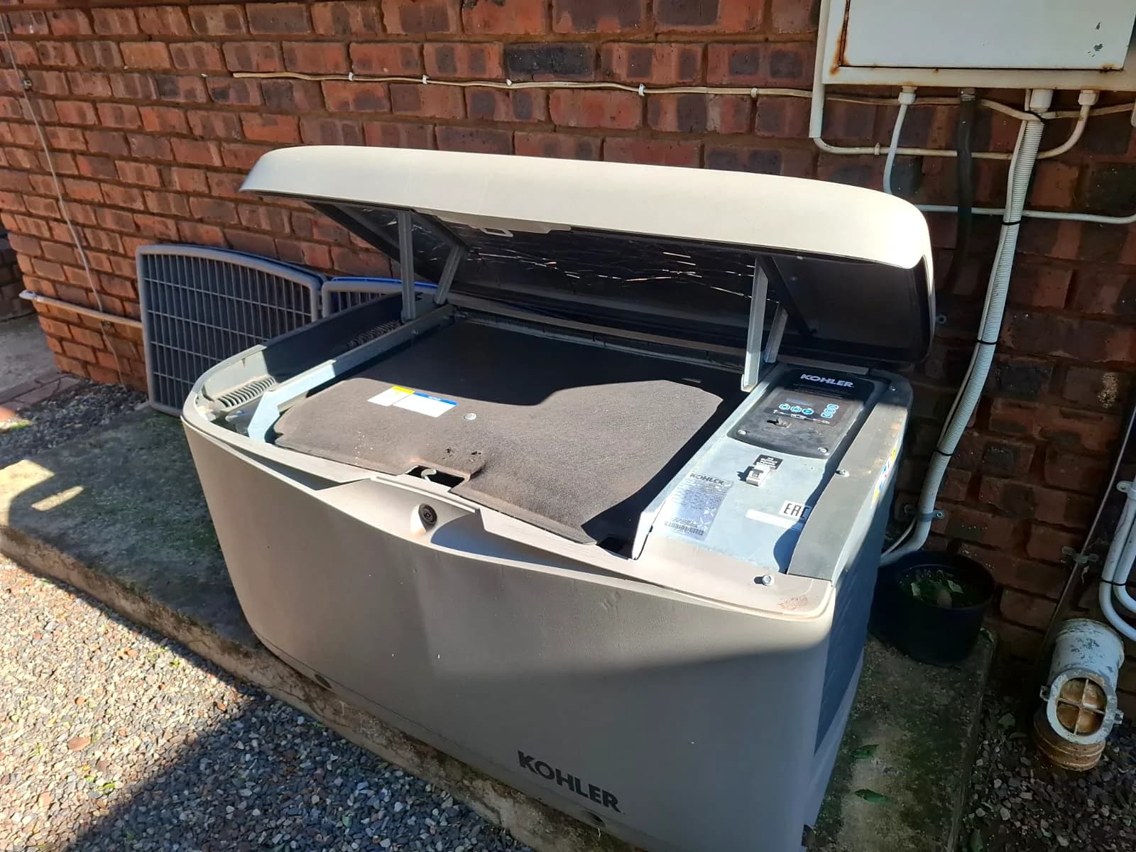 Kohler home standby generator with its lid open beside a brick house wall