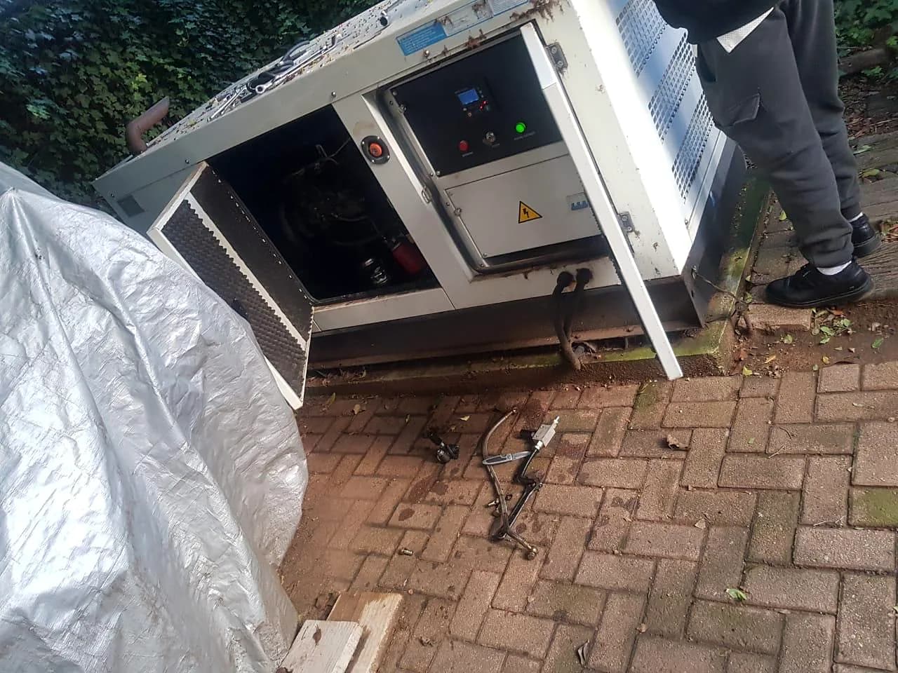 Technician opening the canopy of a silent diesel generator for a repair, with tools laid out on the paving