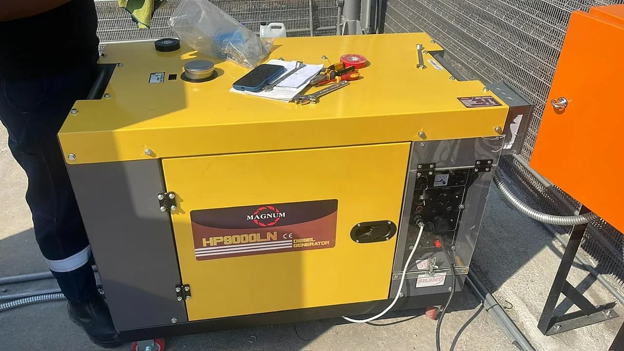 Technician working on a new yellow Magnum silent diesel generator, with tools and tape on its canopy and an orange electrical box beside it